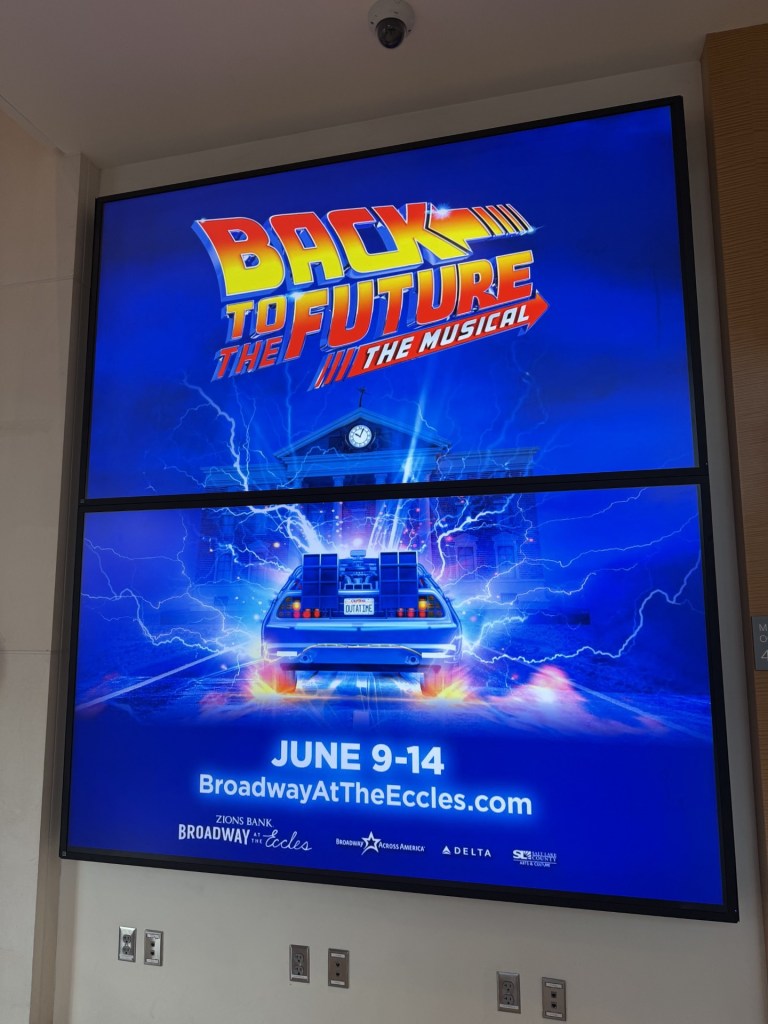 Promotional poster for 'Back to the Future: The Musical' featuring the iconic DeLorean time machine, blue lightning, and details for the event dates from June 9-14 at Broadway at the Eccles.