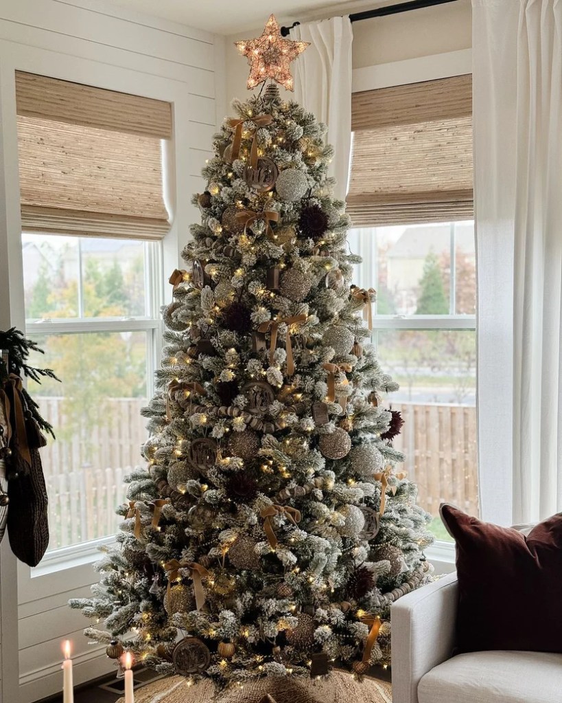 A beautifully decorated Christmas tree with a star on top, adorned with gold ribbons, ornaments, and lights, standing in a cozy living room next to a white couch and candles.