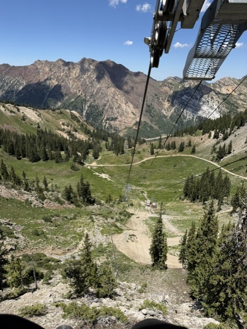 View from a cable car showing a mountainous landscape with green valleys and trees below.