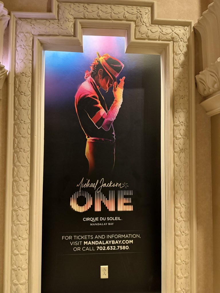 A promotional poster for the Cirque du Soleil show 'Michael Jackson ONE' at Mandalay Bay, featuring a silhouette of a dancer in a fedora and red jacket against a colorful background.