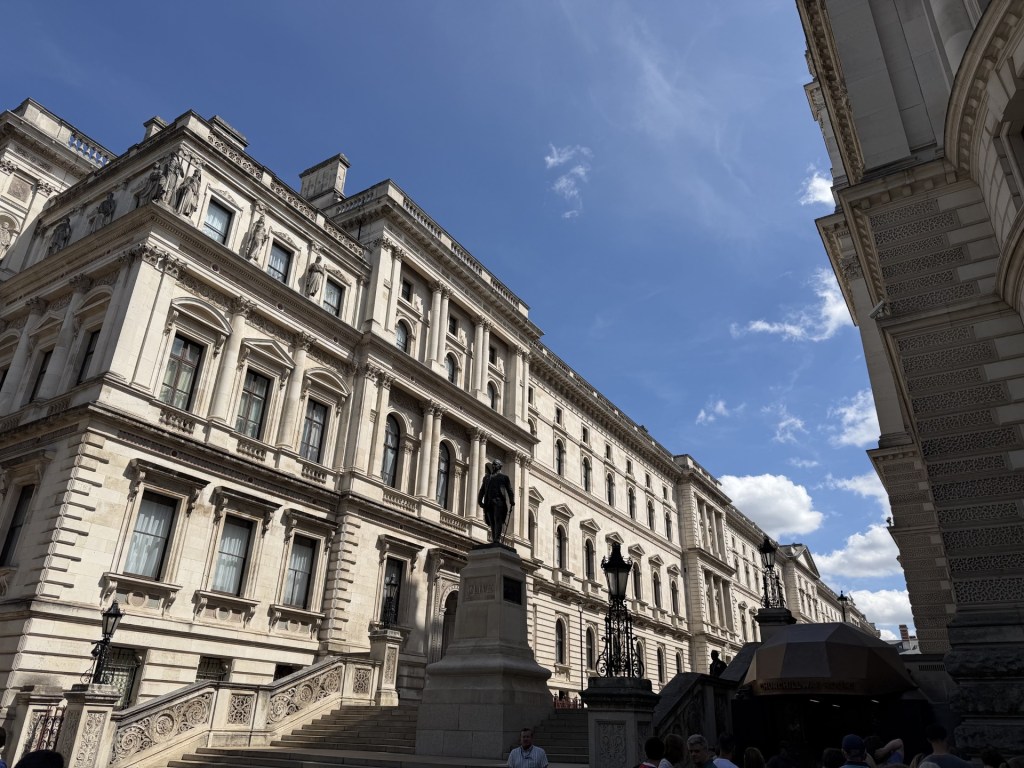 Historic building facade with ornate architecture and a statue in the foreground under a blue sky.