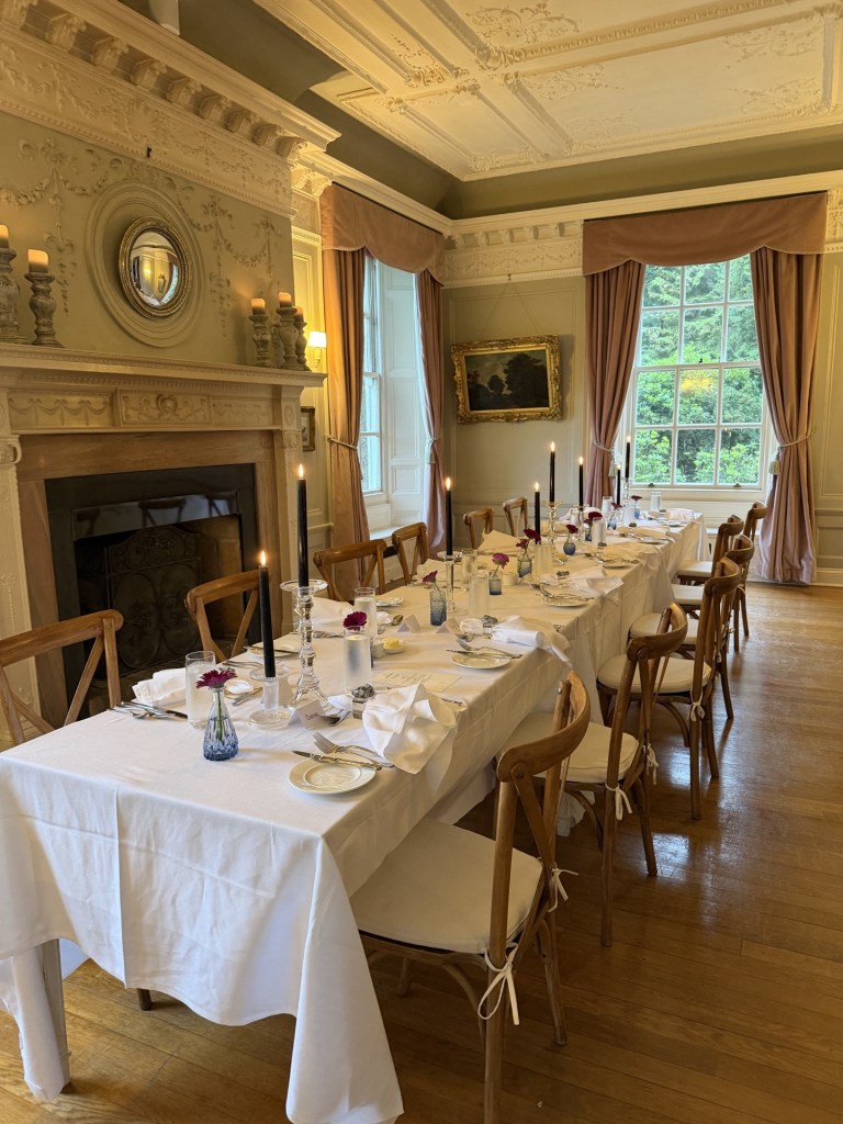 Elegant dining room set for a formal meal with a long table covered in a white tablecloth, adorned with candles and floral arrangements, surrounded by wooden chairs.