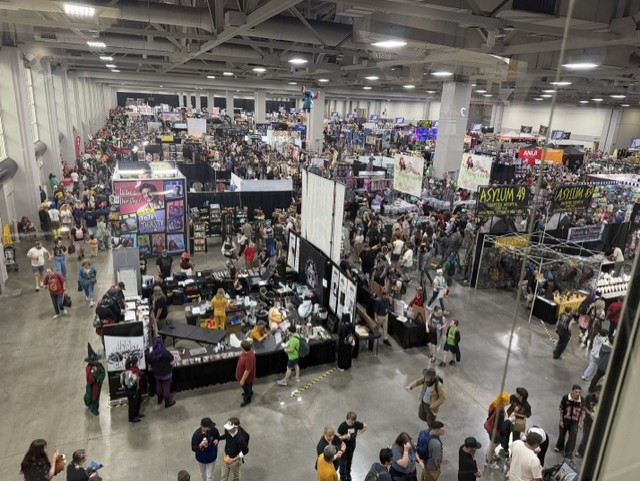 Aerial view of a crowded convention hall filled with vendors and attendees, showcasing booths and displays for various merchandise.