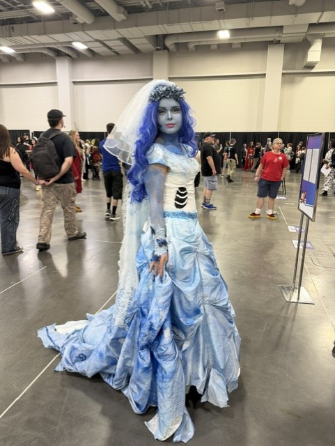 A person in a blue gown and veil, with blue hair and face paint, posing at a convention.