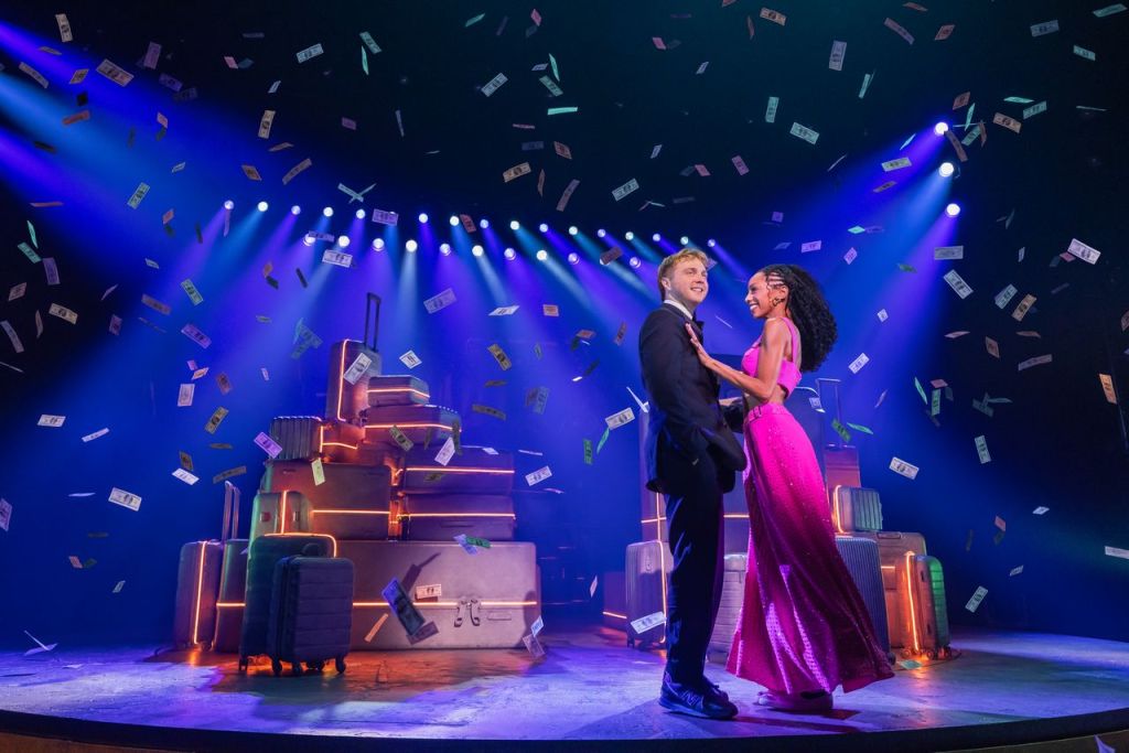 A couple dances on stage surrounded by colorful lights and floating dollar bills, with luggage in the background.